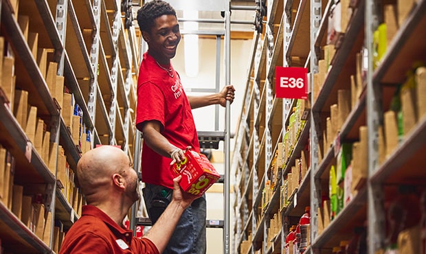 Two Target employees in red shirts stocking shelves, illustrating teamwork in the store's warehouse.